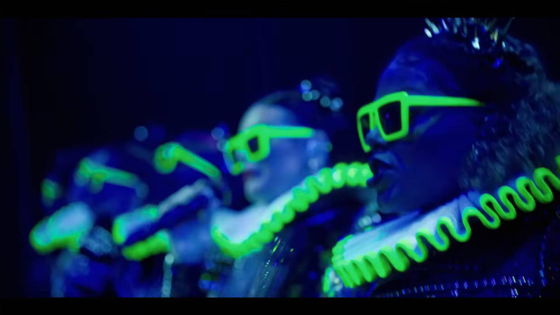 Everything is glowing blue and green because of a blacklight. The cast stands in a line wearing Elizabethan style ruffs and sunglasses. This is for the musical number "Haus of Holbein"